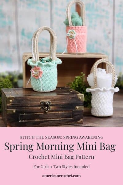 Pinterest style product graphic for the Spring Morning Mini Bag crochet pattern by Mistie Bush of American Crochet. The top portion shows three crocheted mini bags styled on a dark wood treasure chest and wooden crate against a distressed teal wall with greenery. The bags are shown in mint green with ruffle trim and a small crocheted flower button accent, coral pink with a teal rolled rosette, and white with lace ruffle trim and pearl handle detail — all with natural jute style handles. The bottom pink text block reads: Stitch the Season: Spring Awakening — Spring Morning Mini Bag — Crochet Mini Bag Pattern — For Girls • Two Styles Included — americancrochet.com