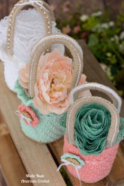 Three crocheted mini bags in mint green and coral pink cotton yarn with jute handles, decorated with fabric flowers and lace details. Spring Morning Mini Bag pattern by Mistie Bush of American Crochet.