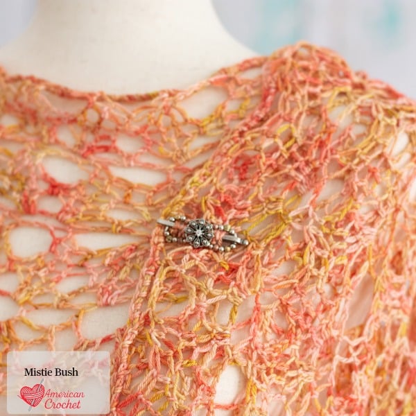 Amber Rose Wrap crochet pattern close-up — delicate open lace mesh stitch detail in warm peachy coral and golden yarn, American Crochet
