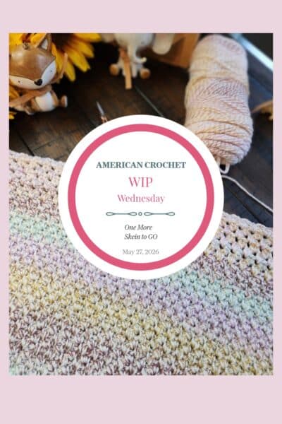 A tall Pinterest image featuring a close-up of a work-in-progress C2C baby blanket in soft rainbow pastel variegated yarn on a dark wood surface. A skein of yarn, ornate scissors, yellow sunflowers, and a wooden fox figurine are visible in the background. A white circle badge in the center reads "American Crochet — WIP Wednesday — One More Skein to Go — May 27, 2026." A soft pink border frames the image.