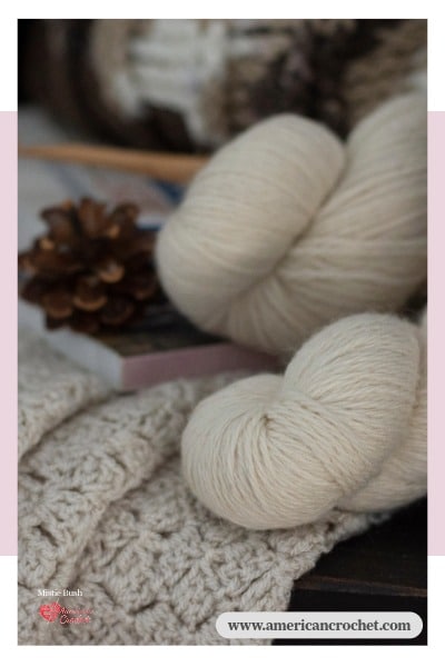 Soft cream yarn skeins resting beside a finished crochet piece, styled with a pinecone — a quiet moment from my craft room at American Crochet.