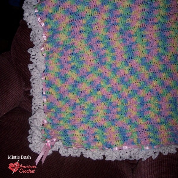 The first baby blanket I ever made as a shower gift — worked in a shell stitch with a white ruffled edge and pink satin ribbon threaded through, made in 2004.