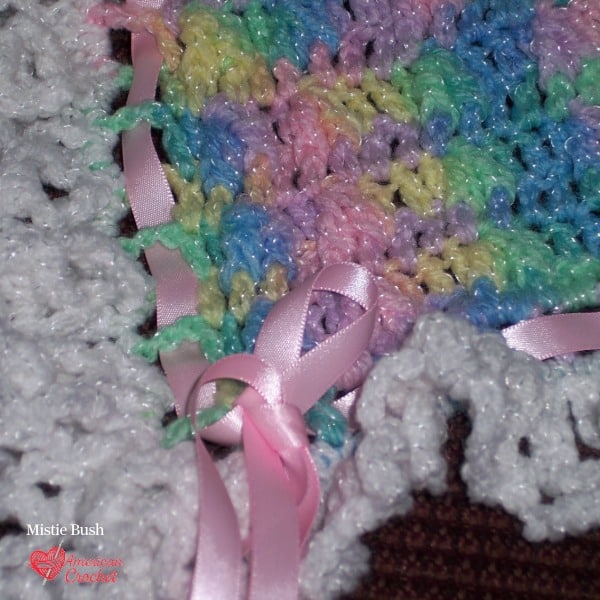 Close-up of a hand-tied pink satin ribbon woven through a white crochet ruffle edge — detail from Mistie Bush's first handmade baby blanket, 2004.