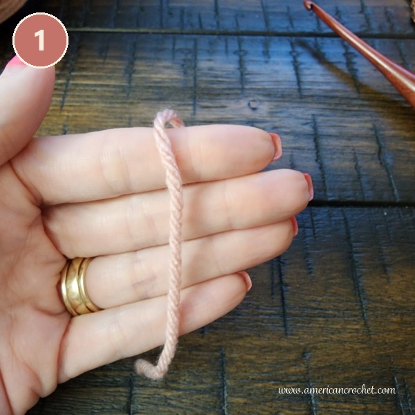 Step 1 - blush pink yarn draped over the hand, ready to make a crochet slip knot.
