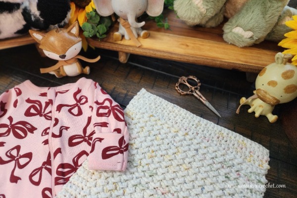 Sophie's Little Blessing Lovey with a pink baby outfit and nursery toys - free crochet pattern from American Crochet.