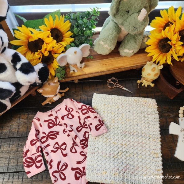 Sophie's Little Blessing Lovey laid out with a pink baby outfit, sunflowers and nursery toys - free preemie crochet pattern.