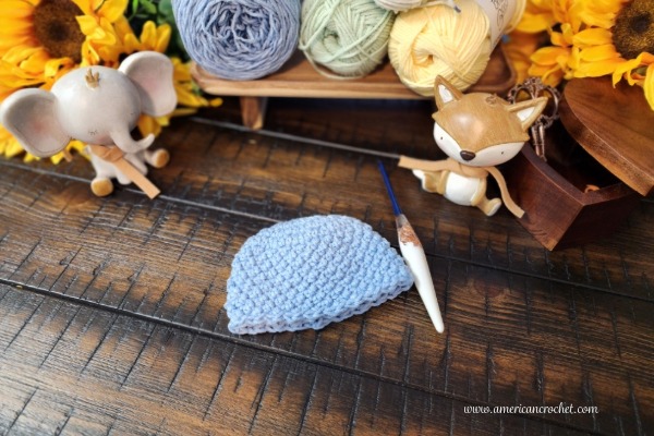 Sophie's Little Blessing Preemie Hat — a soft blue crochet preemie hat styled with pastel yarn cakes, sunflowers, and a little fox, by American Crochet.
